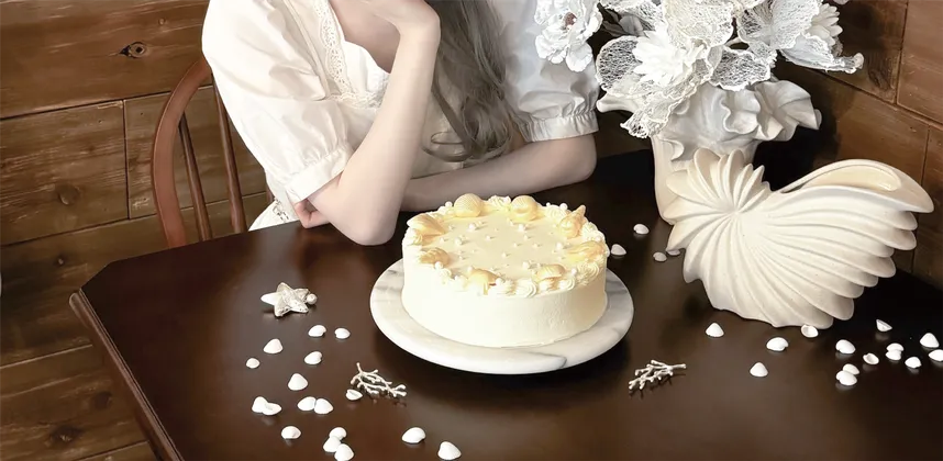 木のテーブルに置かれた白いケーキと、白い衣装のスタッフ。喫茶 微睡の公式掲載写真。